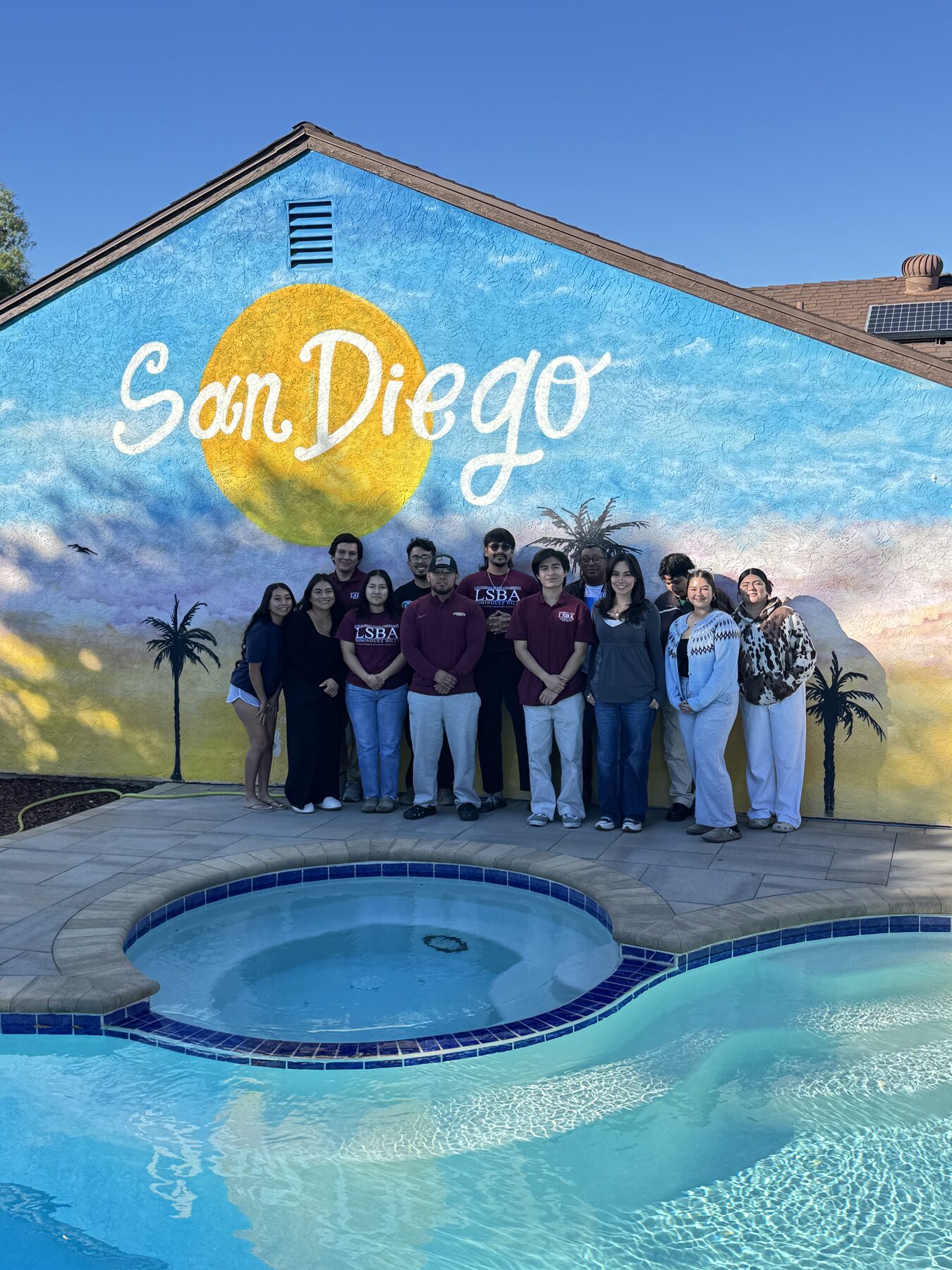 LSBA members in LSBA polos standing by a pool in front of a painted San Diego mural during a chapter trip.
