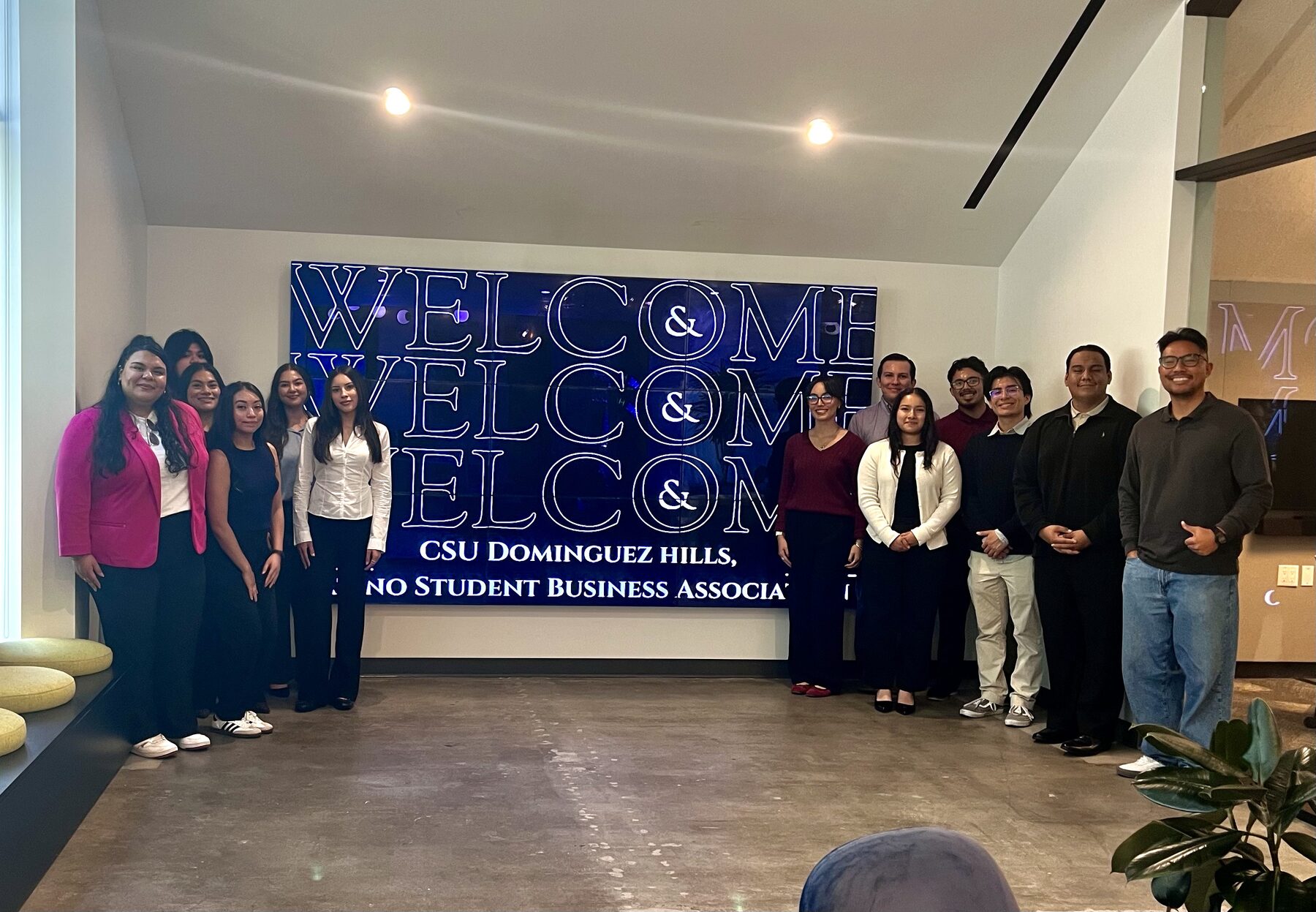 LSBA members standing in front of an illuminated welcome wall reading CSU Dominguez Hills, Latino Student Business Association during a company visit.