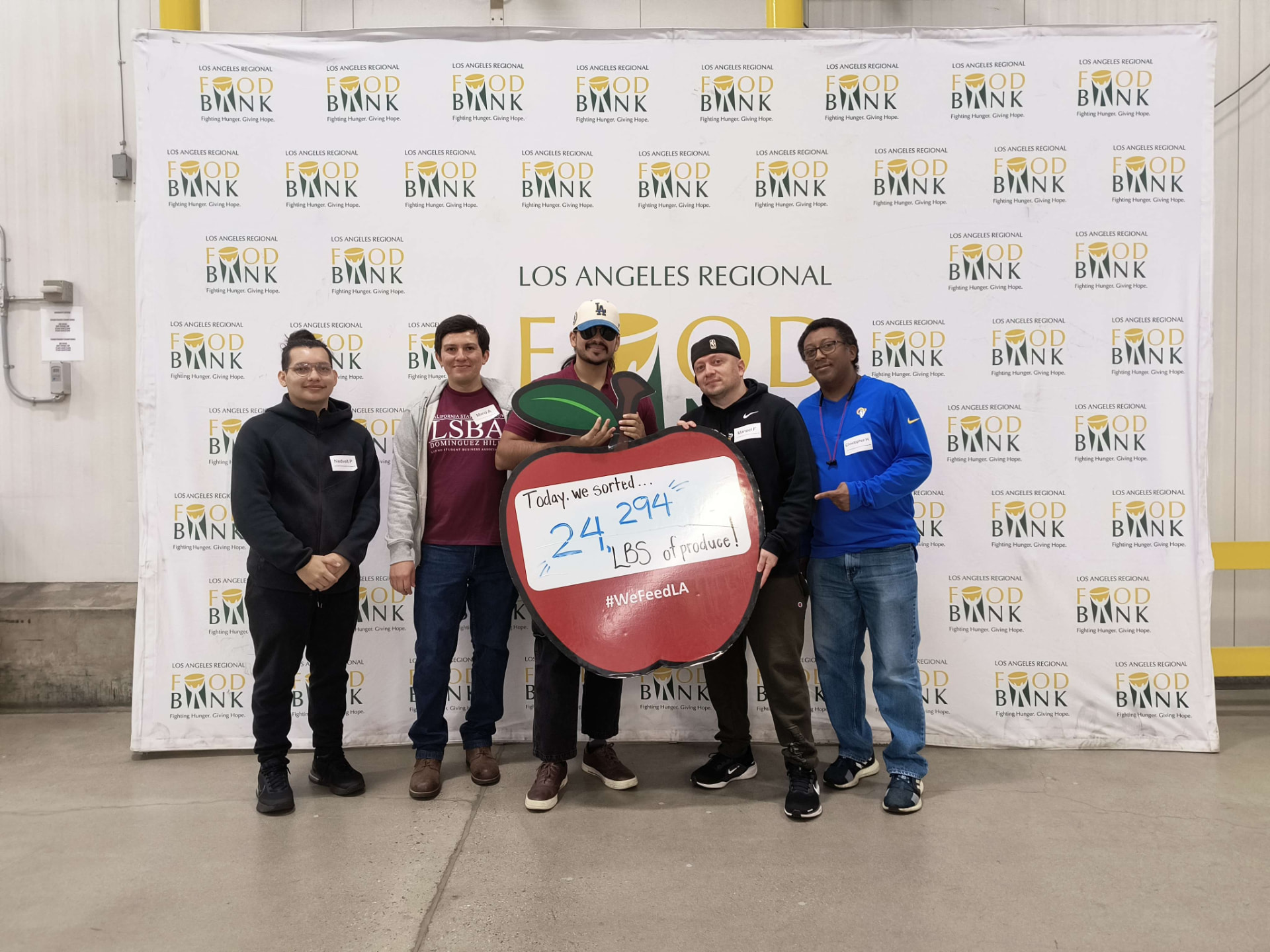 Five LSBA members at the Los Angeles Regional Food Bank holding a sign showing 24,294 lbs of produce sorted.