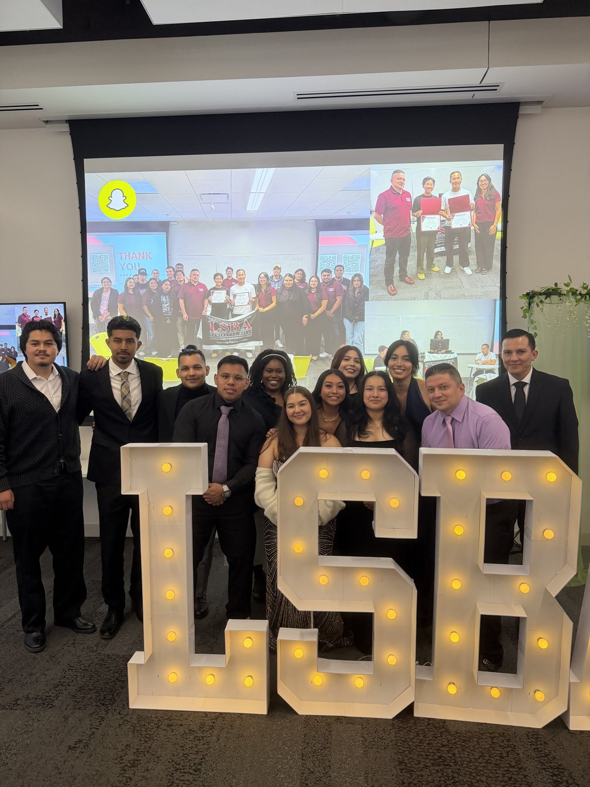 LSBA members in formal attire posing behind large illuminated marquee letters spelling LSBA at the spring banquet.